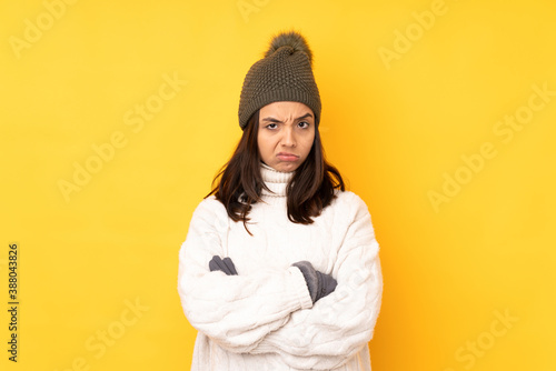 Young woman with winter hat over isolated yellow background feeling upset © luismolinero