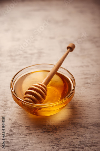 Fresh clear honey in a glass bowl with a ribbed honey stick on a wooden table