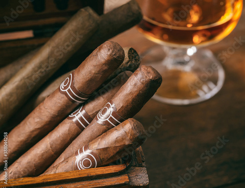Cuban cigars closeup on wooden desk, blur glass of brandy.