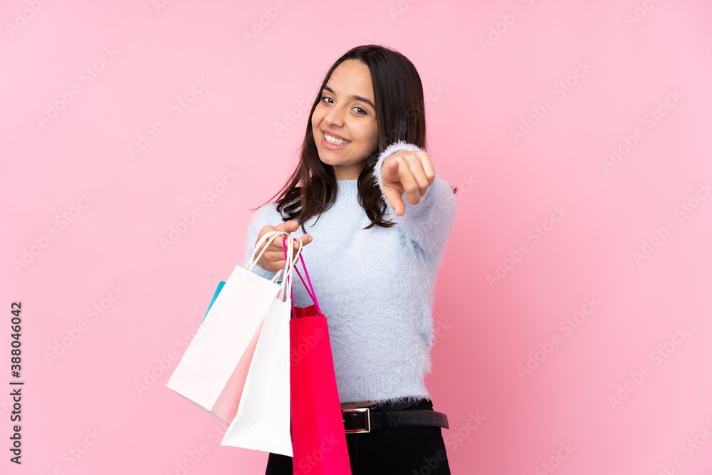 Young woman with shopping bag over isolated pink background points finger at you with a confident expression