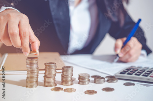 Closeup image businesswoman holding coins putting to stacking coins bank and calculating record or signing on business document. concept saving money wealth for finance accounting.