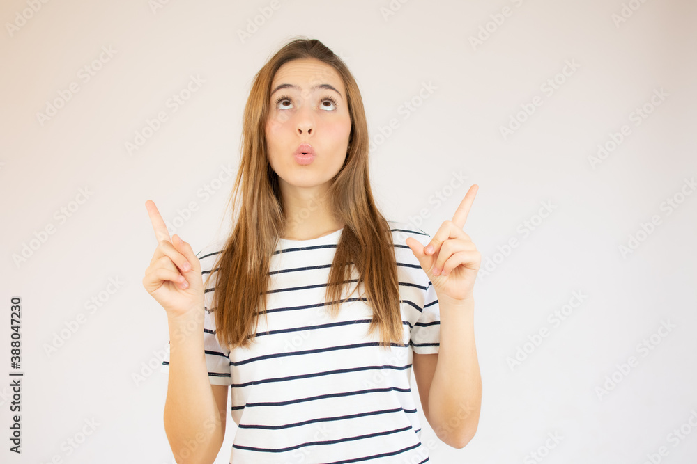 Portrait of a happy young girl dressed in red striped t-shirt pointing fingers up at copy space isolated over white background Portrait of a happy young girl dressed in red striped t-shirt pointing fingers up at copy space isolated over white background