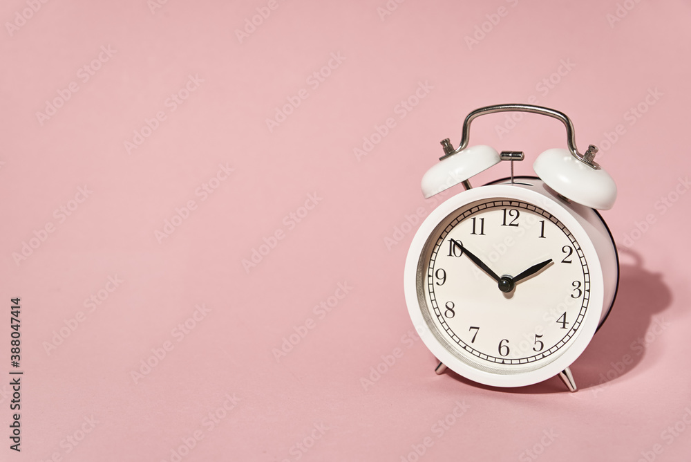White alarm clock and leaves shadows on pastel pink background White alarm clock and leaves shadows on pastel pink background