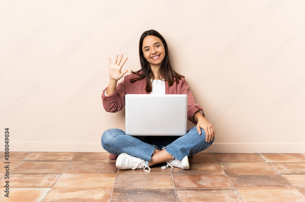 Young mixed race woman with a laptop sitting on the floor counting five with fingers Young mixed race woman with a laptop sitting on the floor counting five with fingers