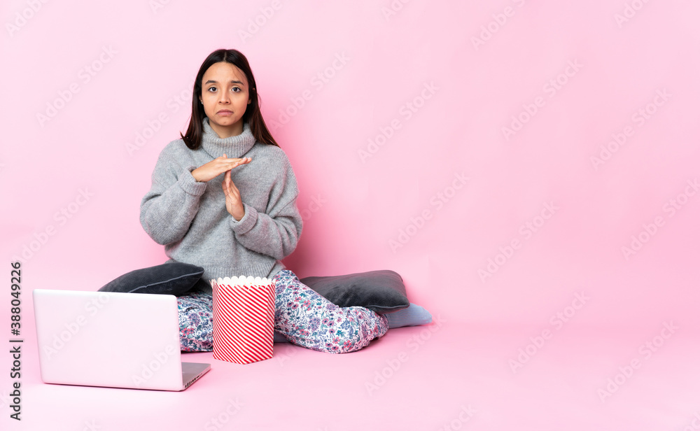 Young mixed race woman eating popcorn while watching a movie on the laptop making time out gesture Young mixed race woman eating popcorn while watching a movie on the laptop making time out gesture