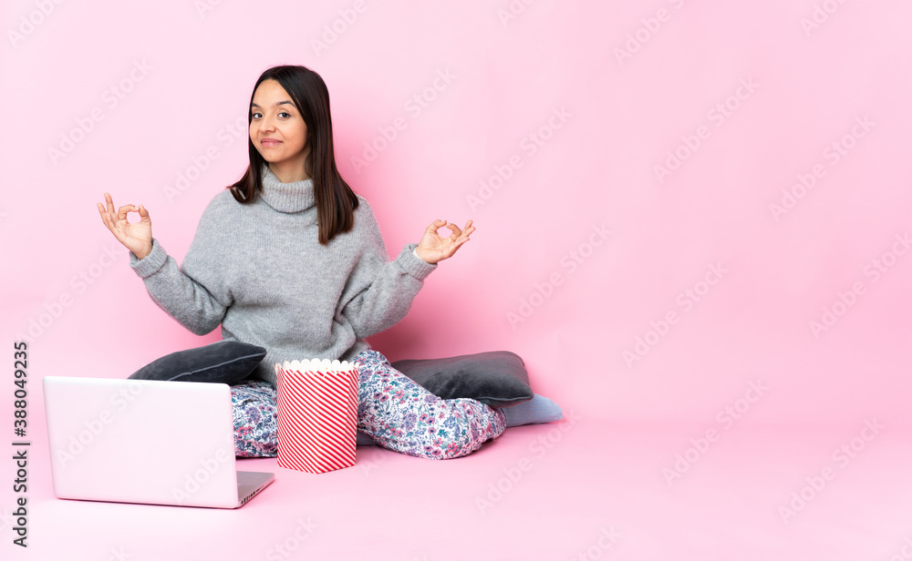 Young mixed race woman eating popcorn while watching a movie on the laptop in zen pose Young mixed race woman eating popcorn while watching a movie on the laptop in zen pose