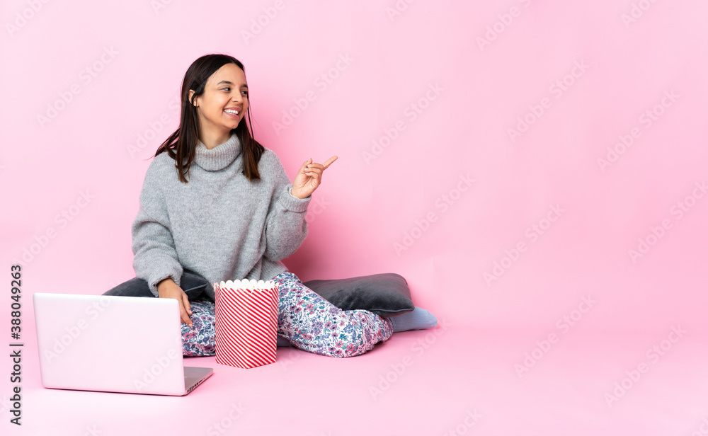 Young mixed race woman eating popcorn while watching a movie on the laptop intending to realizes the solution while lifting a finger up Young mixed race woman eating popcorn while watching a movie on the laptop intending to realizes the solution while lifting a finger up