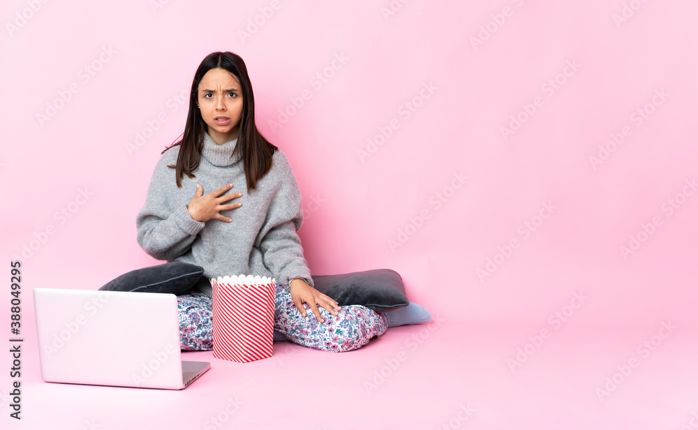 Young mixed race woman eating popcorn while watching a movie on the laptop pointing to oneself Young mixed race woman eating popcorn while watching a movie on the laptop pointing to oneself