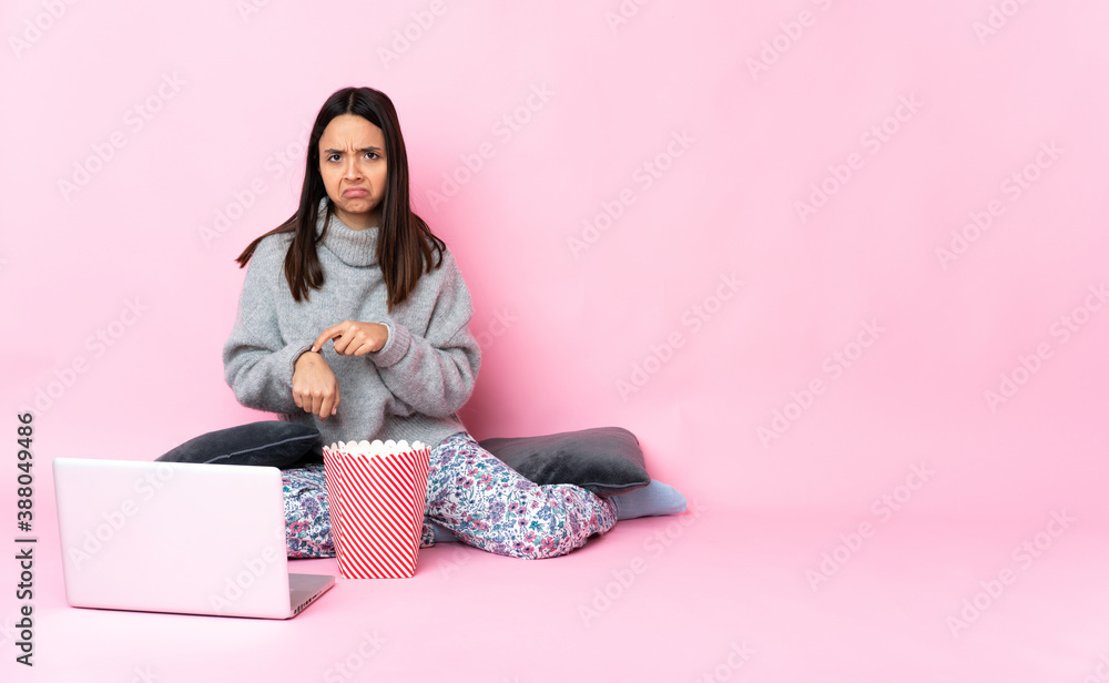 Young mixed race woman eating popcorn while watching a movie on the laptop making the gesture of being late Young mixed race woman eating popcorn while watching a movie on the laptop making the gesture of being late