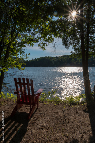 An empty Muskoka (Adirondack) chair casts a relaxing shadow by a small lake near Huntsville, in Ontario's cottage country, in the late afternoon sun.