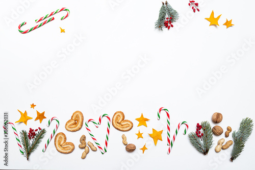 Festive Christmas composition of fir branches, berries, nuts, candy canes, cookies and stars on a white background. Colorful Christmas ornament with space for text flat lay