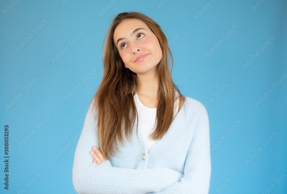Teenager girl over blue wall making doubts gesture while crossed arms. Teenager girl over blue wall making doubts gesture while crossed arms.