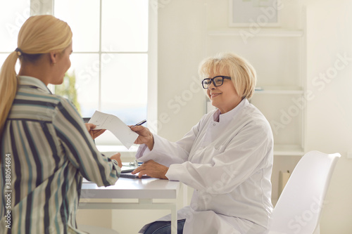 Friendly senior female doctor gives a prescription to a patient in his office.