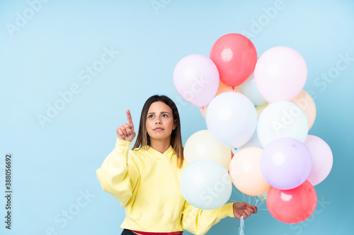 Woman holding balloons in a party over isolated blue background touching on transparent screen © luismolinero