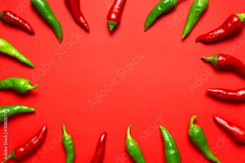 Frame made of Hot red and green fresh chili peppers on red background flat lay top view. Seasoning for dish, spicy spices for cooking, cayenne pepper, food. Creative layout, chili pattern