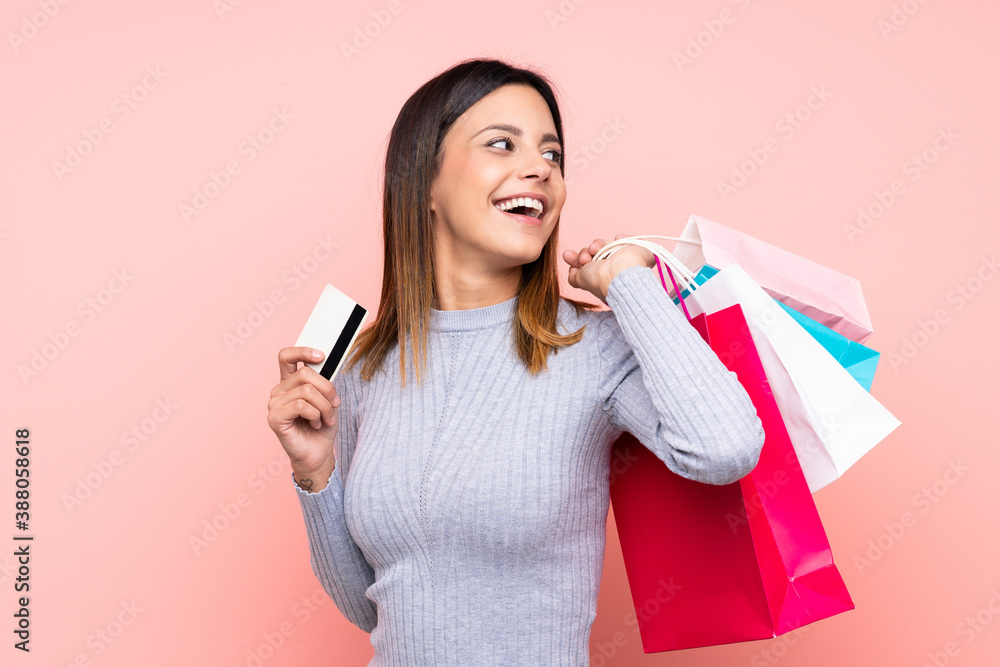 Woman over isolated pink background holding shopping bags and a credit card Woman over isolated pink background holding shopping bags and a credit card
