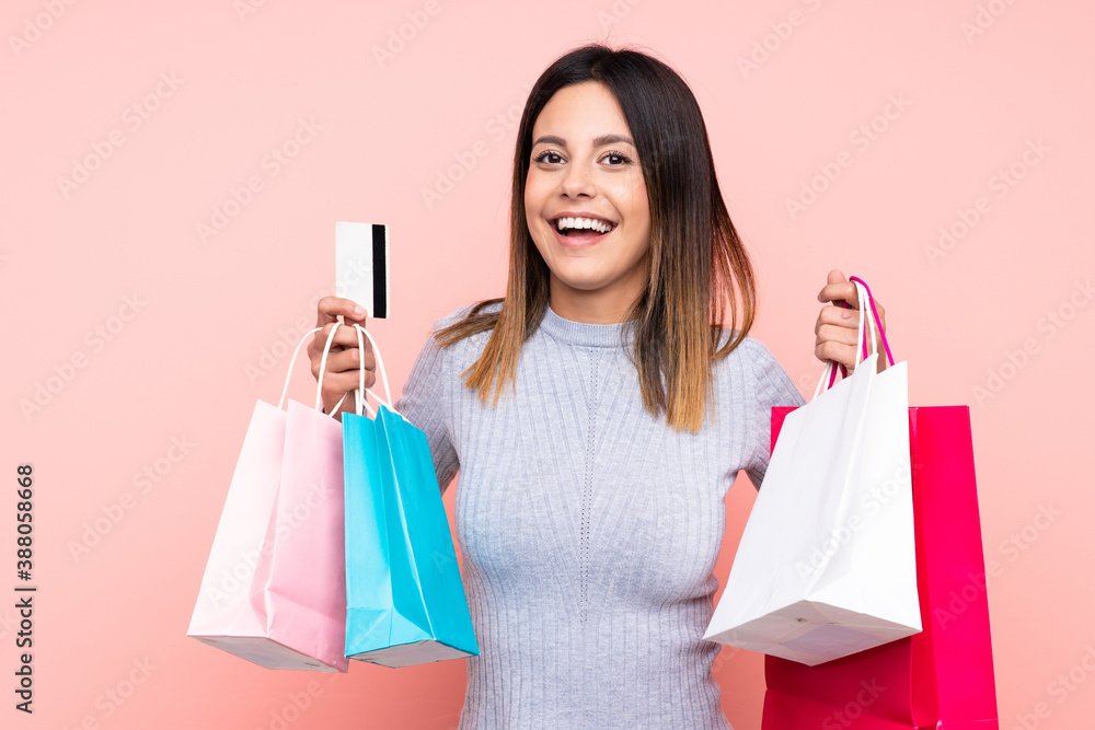 Woman over isolated pink background holding shopping bags and surprised