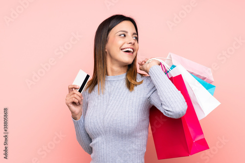 Woman over isolated pink background holding shopping bags and a credit card