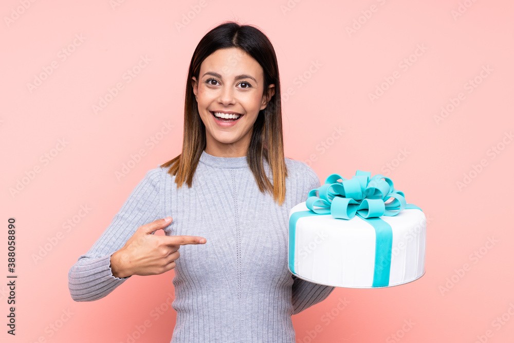 Woman holding a big cake over isolated pink background with surprise facial expression