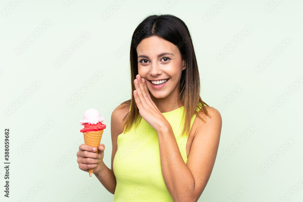 Brunette woman holding a cornet ice cream over isolated green background whispering something Brunette woman holding a cornet ice cream over isolated green background whispering something