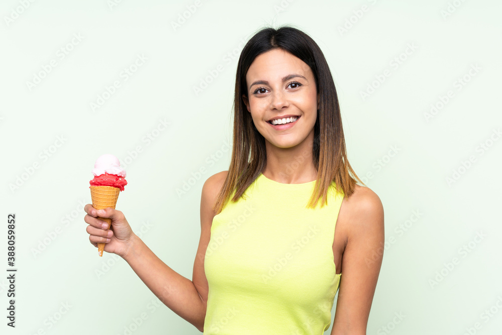 Brunette woman holding a cornet ice cream over isolated green background smiling a lot Brunette woman holding a cornet ice cream over isolated green background smiling a lot