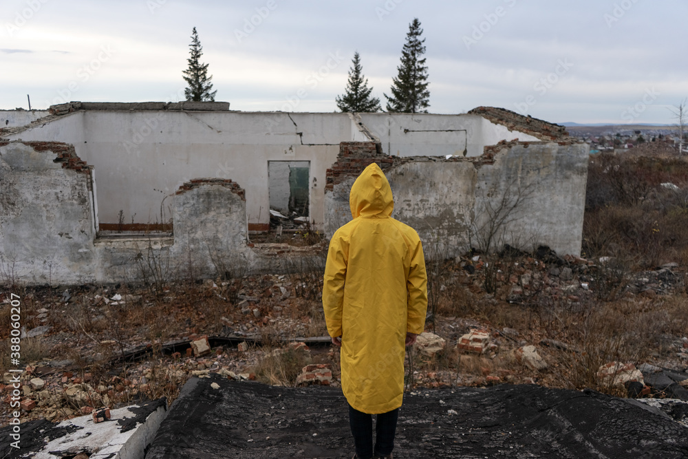a man in a yellow protective cloak stands among the destroyed building. place after a man-made disaster and fire