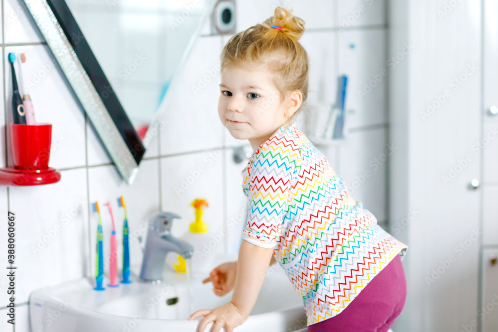 Cute little toddler girl washing hands with soap and water in bathroom. Adorable child learning cleaning body parts. Hygiene routine action during viral desease. kid at home or nursery. Cute little toddler girl washing hands with soap and water in bathroom. Adorable child learning cleaning body parts. Hygiene routine action during viral desease. kid at home or nursery.
