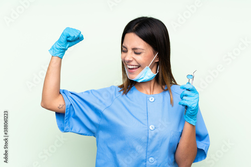 Woman dentist holding tools over isolated green background making strong gesture