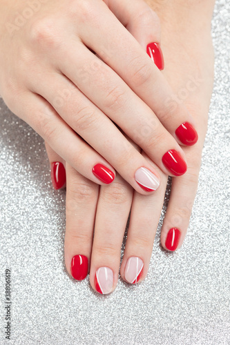 Perfect fingernails of a young woman covered with red  pink and white nail polish on a silver glitter background. Selective focus