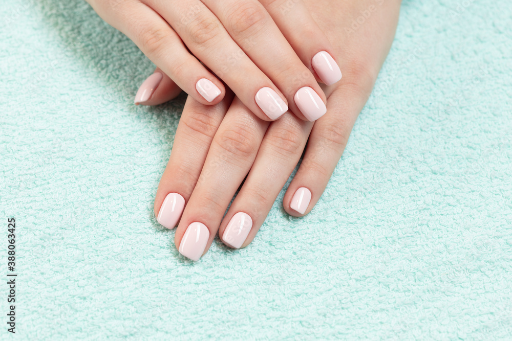Naklejka premium Female hands with new manicure. Hands with pink nail polish on a colored towel. Care for woman hands. Woman in salon receiving manicure by nail beautician. 