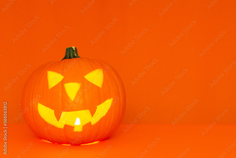 Glowing Halloween pumpkin head jack lantern on trendy orange table background copy space Glowing Halloween pumpkin head jack lantern on trendy orange table background copy space