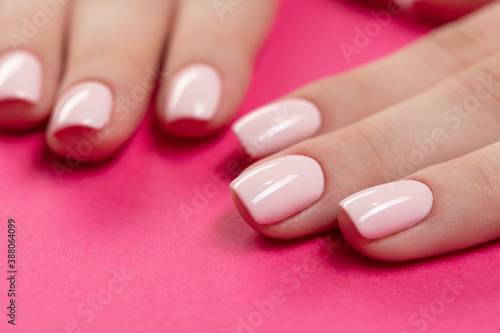 Female hands with new manicure. Hands with pink nail polish on a pink background. Care for woman hands. Woman in salon receiving manicure by nail beautician.