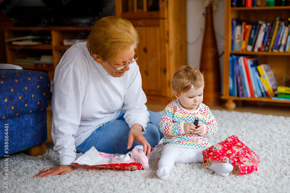 Cute little toddler girl and grandmother playing with toys at home. Adorable baby child and senior retired woman unpacking gifts for birthday. Happy family together Cute little toddler girl and grandmother playing with toys at home. Adorable baby child and senior retired woman unpacking gifts for birthday. Happy family together