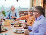 Cheerful senior friends enjoy dinner together on patio at home - Food and drink