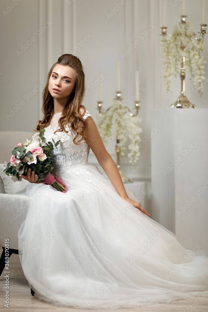 beautiful tender young bride in a luxurious wedding dress with flower bouquet sitting on armchair in white studio interior beautiful tender young bride in a luxurious wedding dress with flower bouquet sitting on armchair in white studio interior