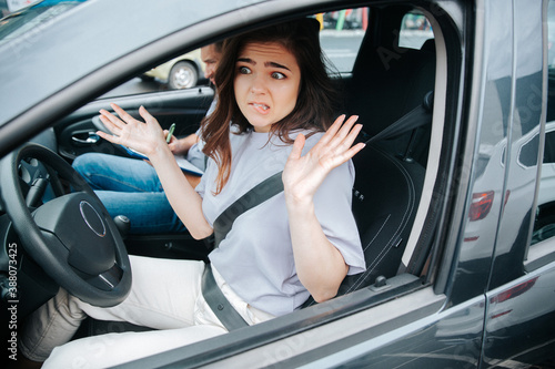 Lovely young woman is troubled with results of driving lesson. Attractive confused woman shrugs up or makes a helpless gesture after making a mistake. Novice driver concept.