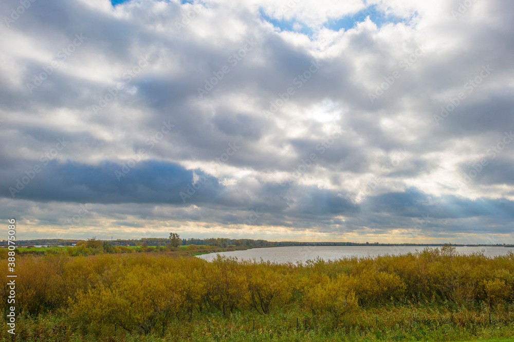 The edge of a lake in autumn colors under a cloudy sky at fall, Almere, Flevoland, The Netherlands, October 26, 2020