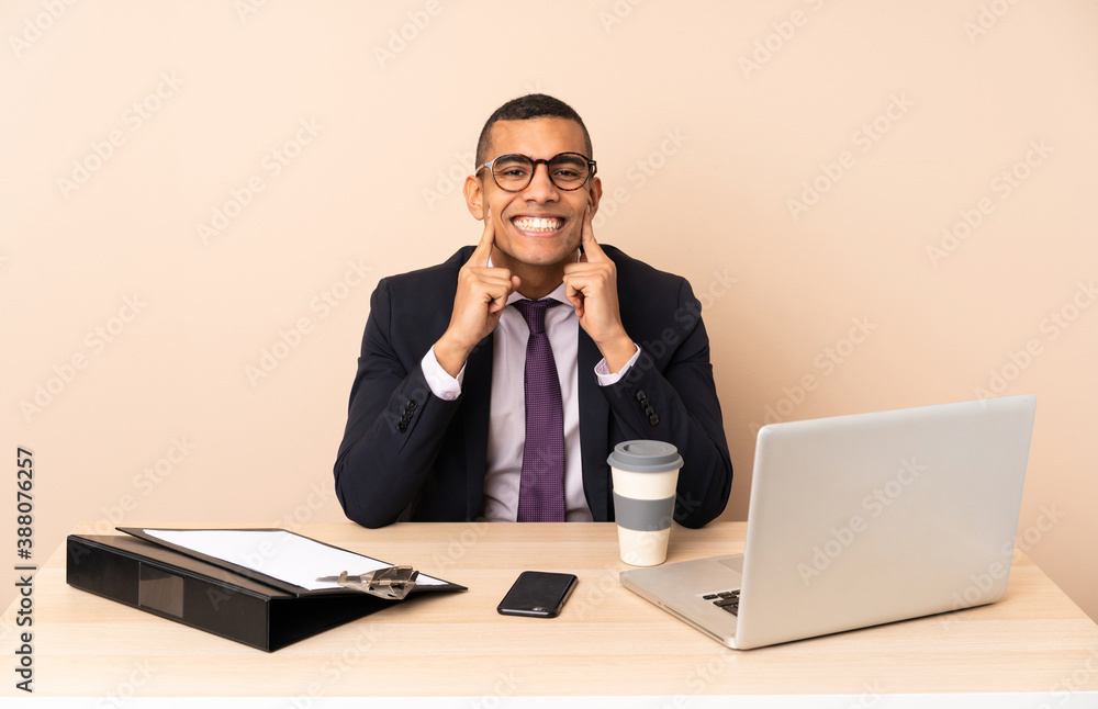 Young business man in his office with a laptop and other documents smiling with a happy and pleasant expression Young business man in his office with a laptop and other documents smiling with a happy and pleasant expression