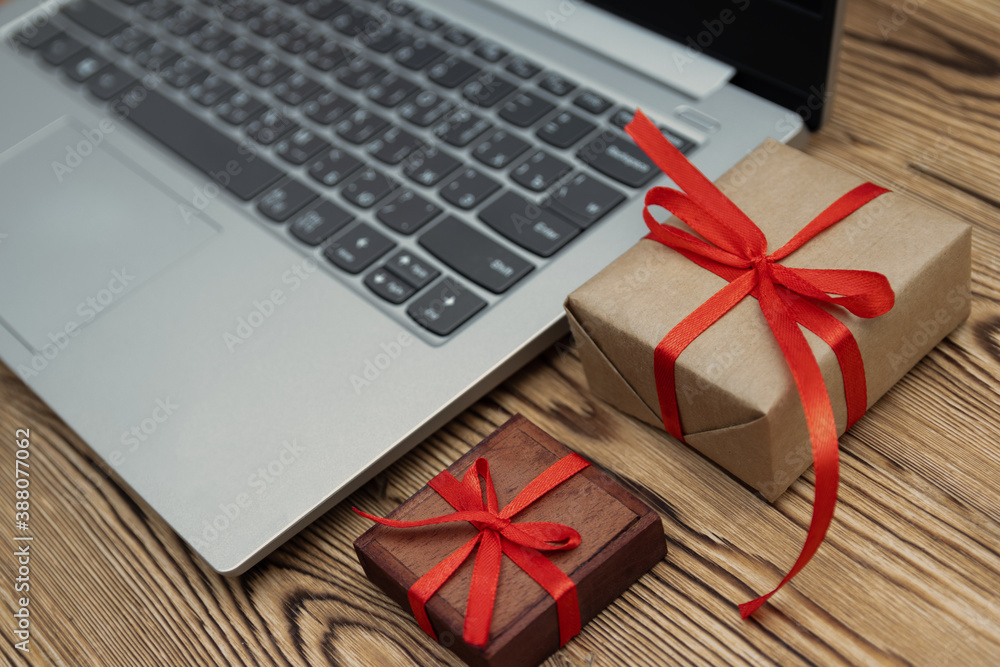 Online shopping for christmas, gift boxes with red ribbon, laying next to a laptop on a wooden table, ordering gifts online, online raffle prizes, copy space Online shopping for christmas, gift boxes with red ribbon, laying next to a laptop on a wooden table, ordering gifts online, online raffle prizes, copy space
