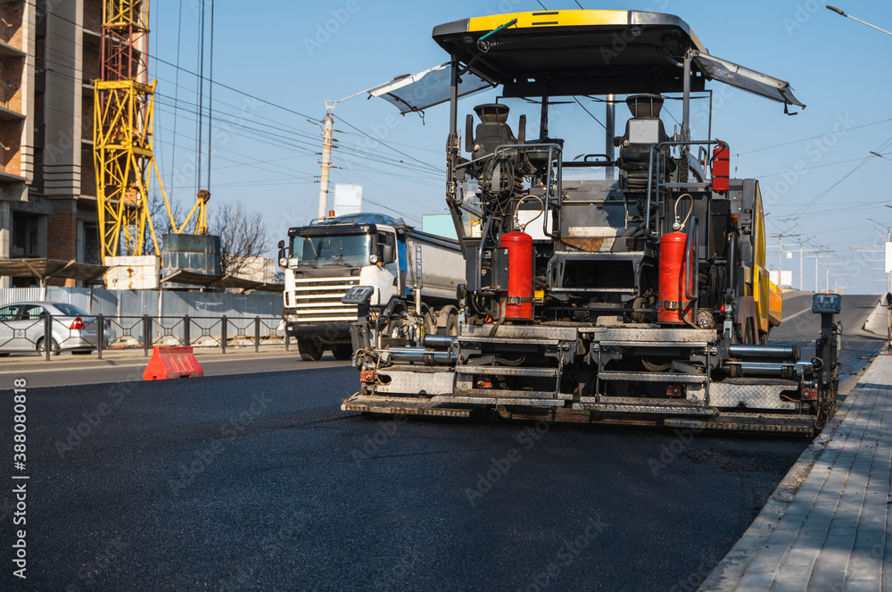Industrial asphalt paver machine laying fresh asphalt on road construction site on the street. A Paver finisher placing a layer of a new hot asphalt on the roadway on a construction site. Repairing.