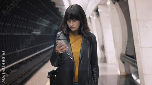 Young asian woman using phone walk along the platform with train arriving. Gimbal shot of woman with phone waiting for the train to come