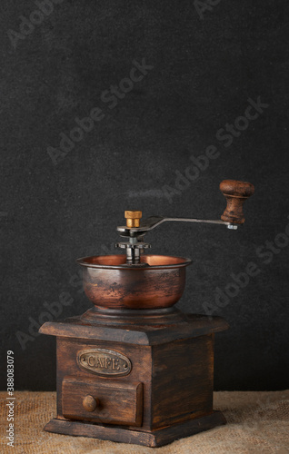 Old vintage grinder with roasted coffee beans and grind coffee in tin jar with scoop over black table with black wooden background. Dark still life