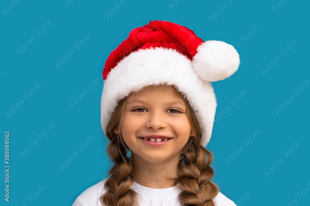 A girl in a Christmas hat poses on a blue background. A girl in a Christmas hat poses on a blue background.