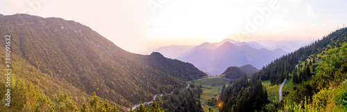 Scenic sunrise panorama in the bavarian alps with dark green forest in the foreground and hiking trails