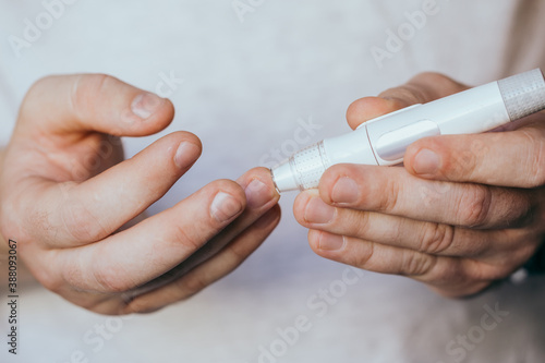 Medicine, diabetes, glycemia, healthcare and people concept - close up of a man's hands using a lancet on his finger to check blood glucose meter with copy space for text