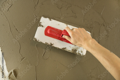 Wallpaper Mural A worker plasters the wall with a spatula and applies a cement mix solution. The repairman lays the plaster on the drywall. Handyman repairs home. Laborer restore dwelling. Specialist covers up cracks Torontodigital.ca