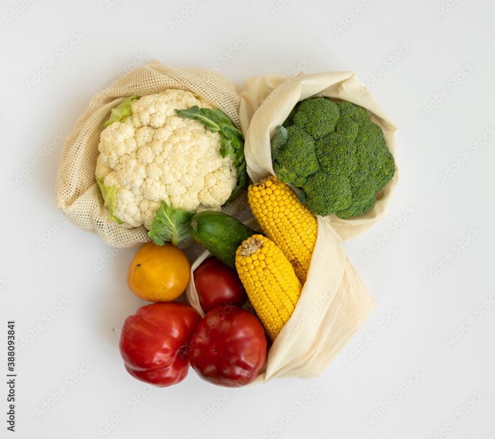 Vegetables in eco bag on white surface. Pepper, tomato, corn, cucumber, broccoli, cauliflower in reusable shopping eco friendly cotton fabric bags. Zero waste and plastic free concept. Sustainable. Vegetables in eco bag on white surface. Pepper, tomato, corn, cucumber, broccoli, cauliflower in reusable shopping eco friendly cotton fabric bags. Zero waste and plastic free concept. Sustainable.