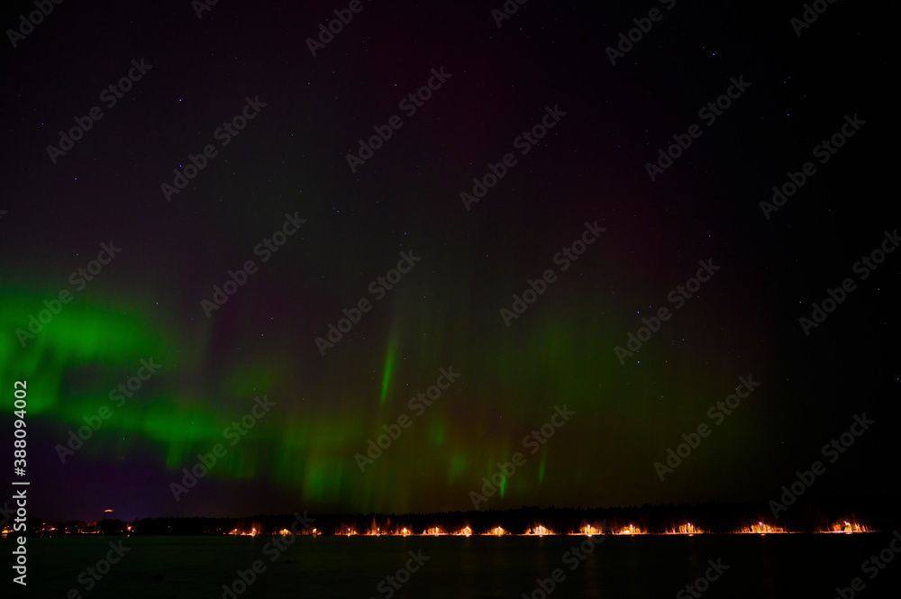A tranquil view of Aurora borealis green beam of northern lights with purple tail beside a lake under starry sky