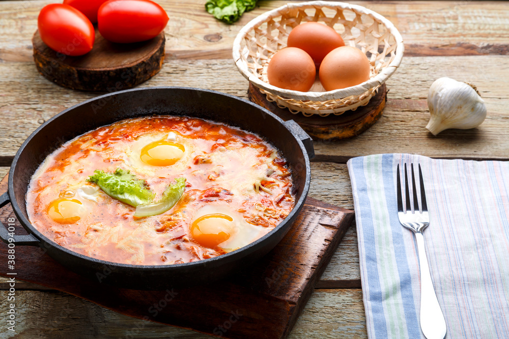 israeli fried eggs shakshuka with cheese in a frying pan next to a fork and a napkin. israeli fried eggs shakshuka with cheese in a frying pan next to a fork and a napkin.
