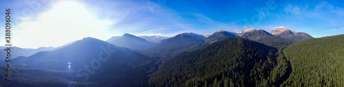 Bright sun rising over the mountains. Panorama of mountain landscape and dense forest from aerial view.